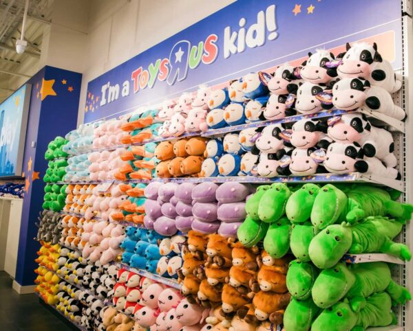 Colorful plush animals stacked on shelves under an “I’m a Toys R Us kid!” wall sign