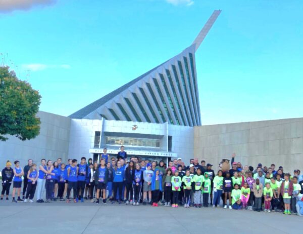 Young Marines and adults in matching shirts posed in front of the National Museum of the Marine Corps entrance and mast