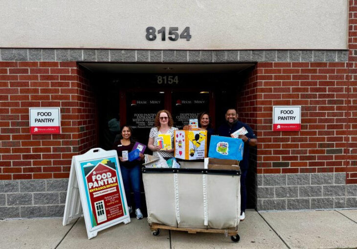Four people stand at the House of Mercy food pantry doors under the 8154 address, holding school-supply donations next to a labeled FOOD PANTRY sign.